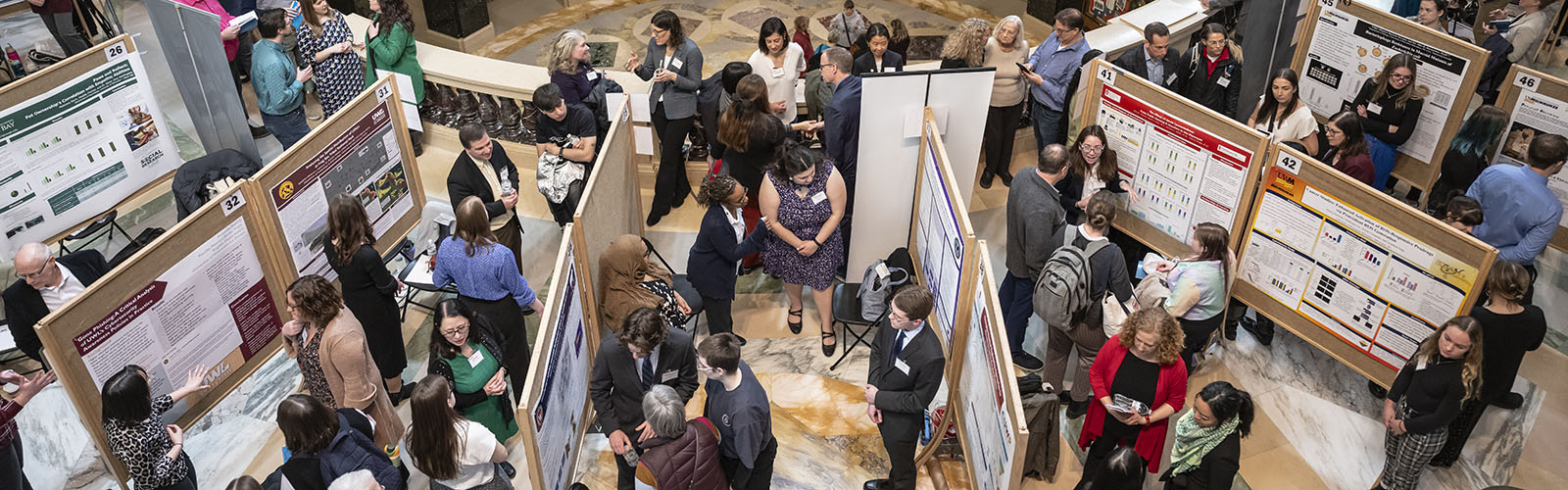 An overhead view of a large number of people presenting and viewing student's research posters in the madison wisconsin state capitol.