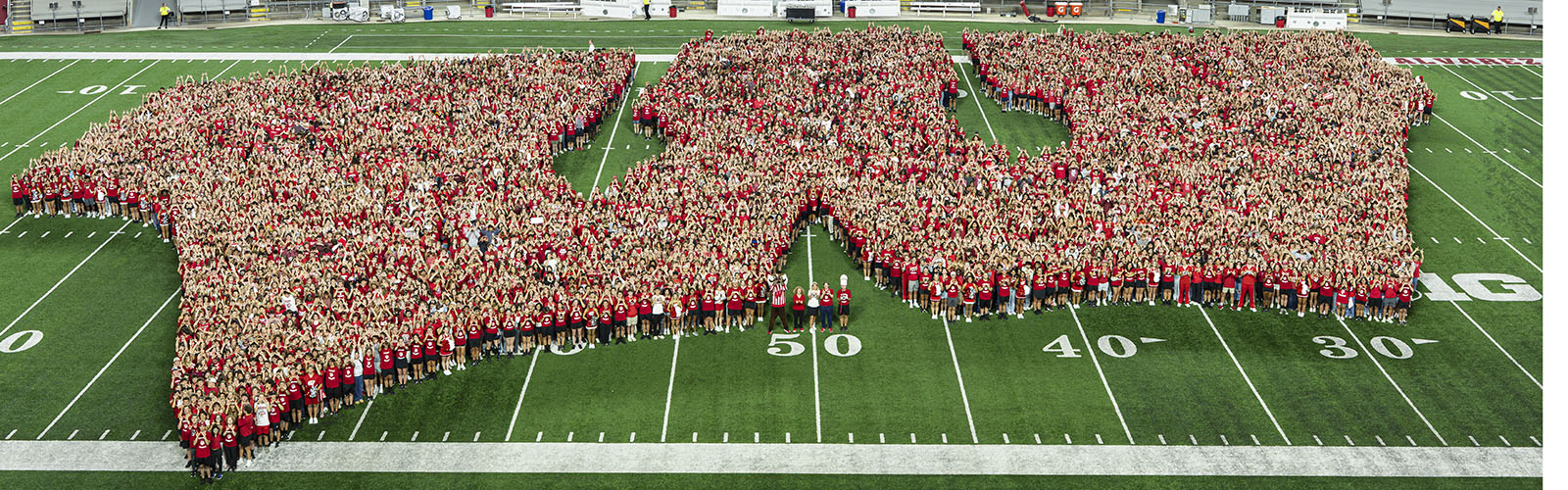 Several thousand first year students standing in the shape of a W on the Camp Randall football field.